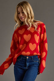 Woman wearing a red sweater with orange heart patterns against a gray background
