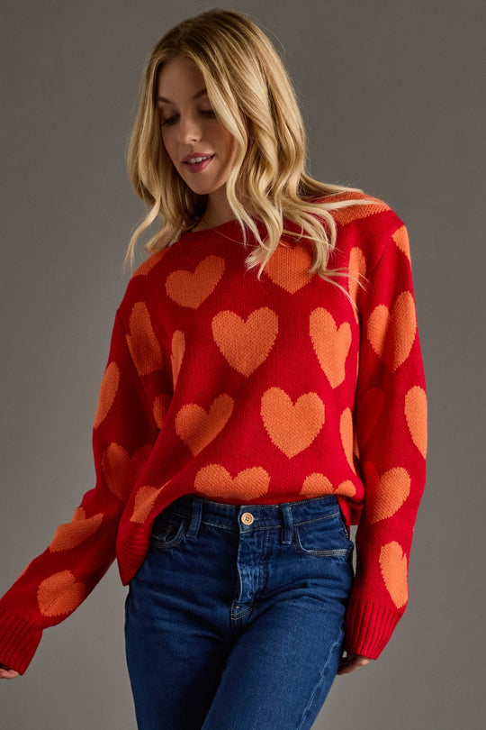 Woman wearing a red sweater with orange heart patterns against a gray background