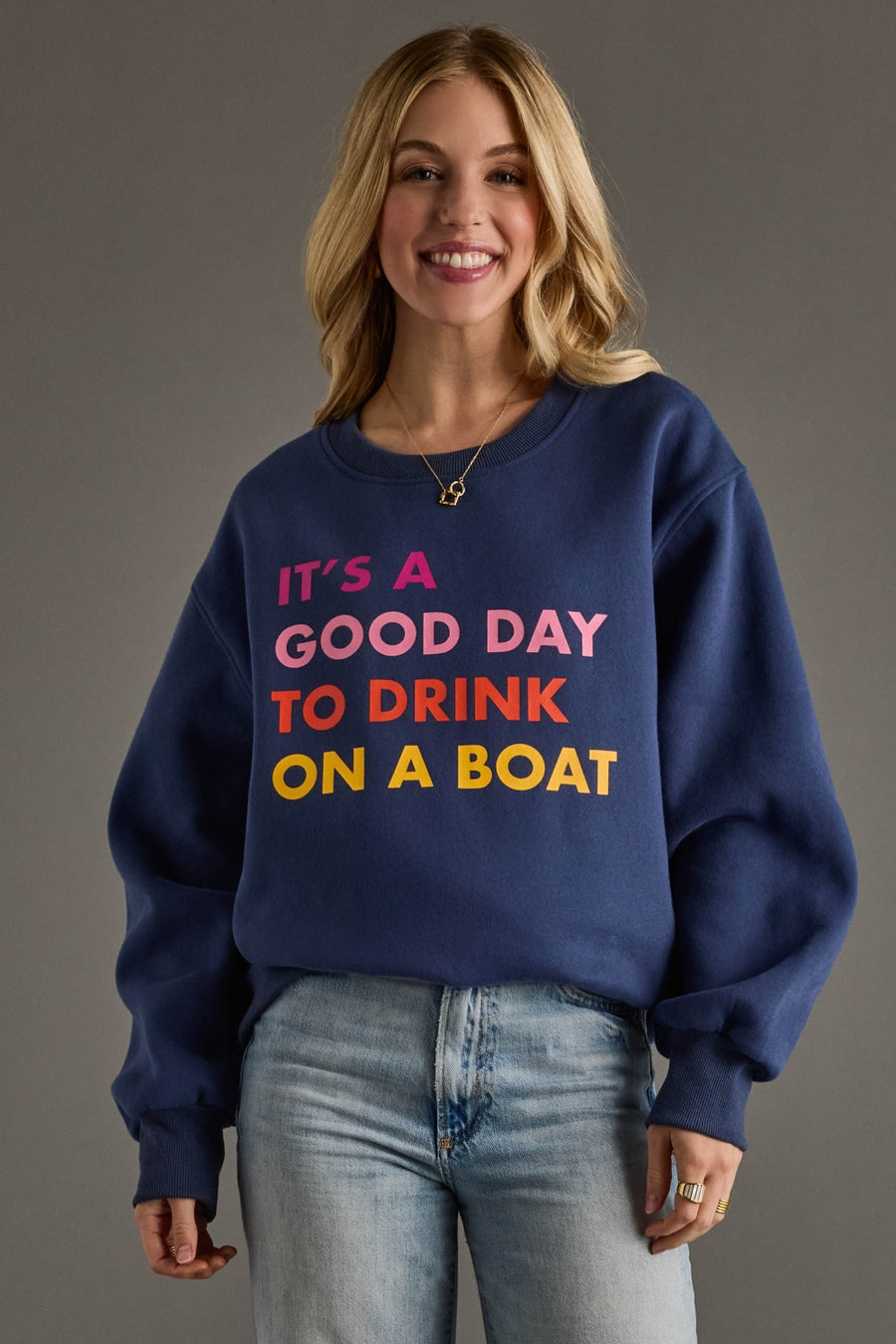 Woman wearing a navy blue sweatshirt with colorful text on a gray background