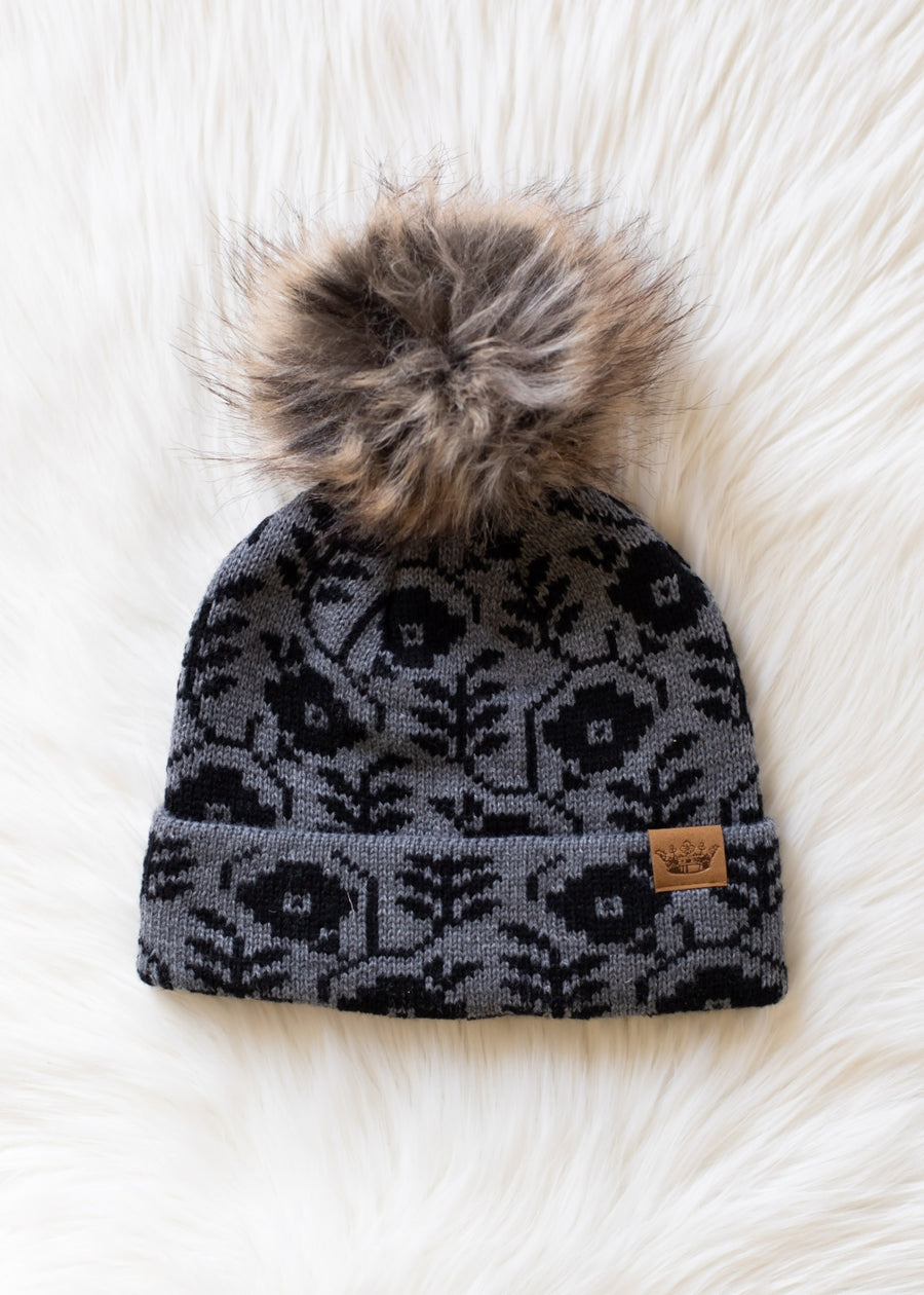 Gray patterned beanie with a fur pom-pom on a white fur surface