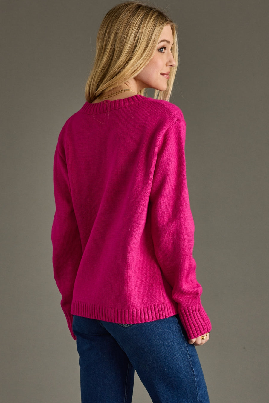 Person wearing a bright pink sweater and blue jeans on a gray background