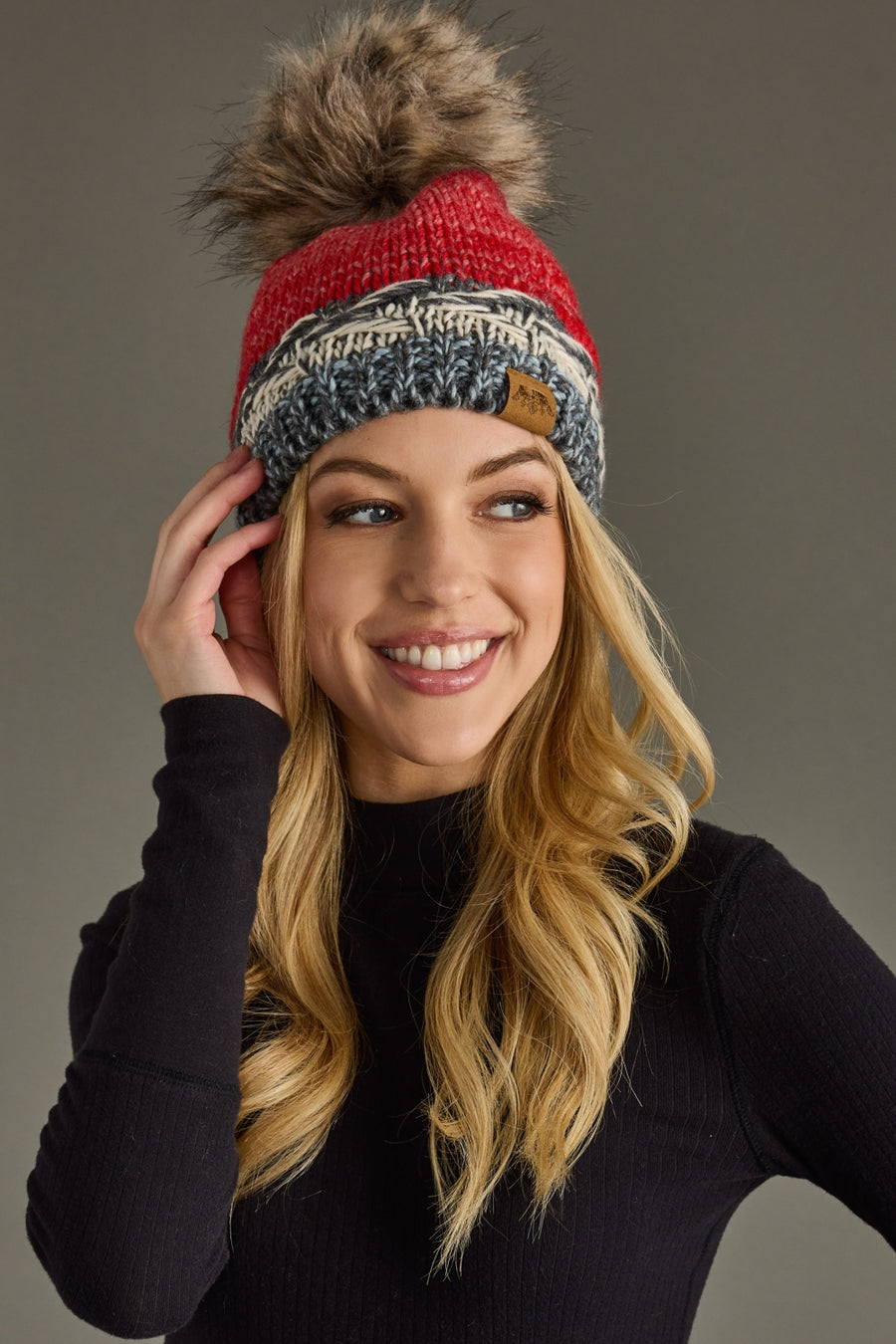 Woman wearing a red and gray knit beanie with a pom-pom on a gray background