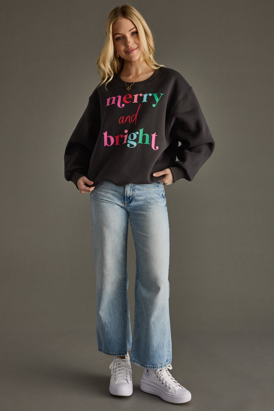 Woman wearing a black sweatshirt with colorful text and blue jeans on a gray background