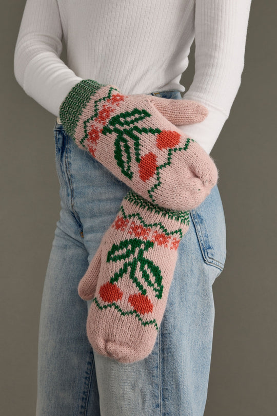 Knitted mittens with floral pattern worn by a person in jeans against a neutral background