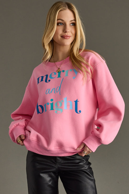 Person wearing a pink sweatshirt with 'merry and bright' text on a gray background