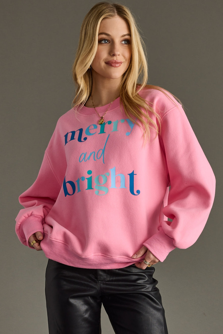 Person wearing a pink sweatshirt with 'merry and bright' text on a gray background