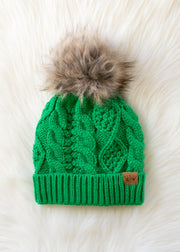 Green knitted beanie with a fur pom-pom on a white fur surface