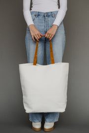 Person holding a white tote bag with brown handles against a gray background