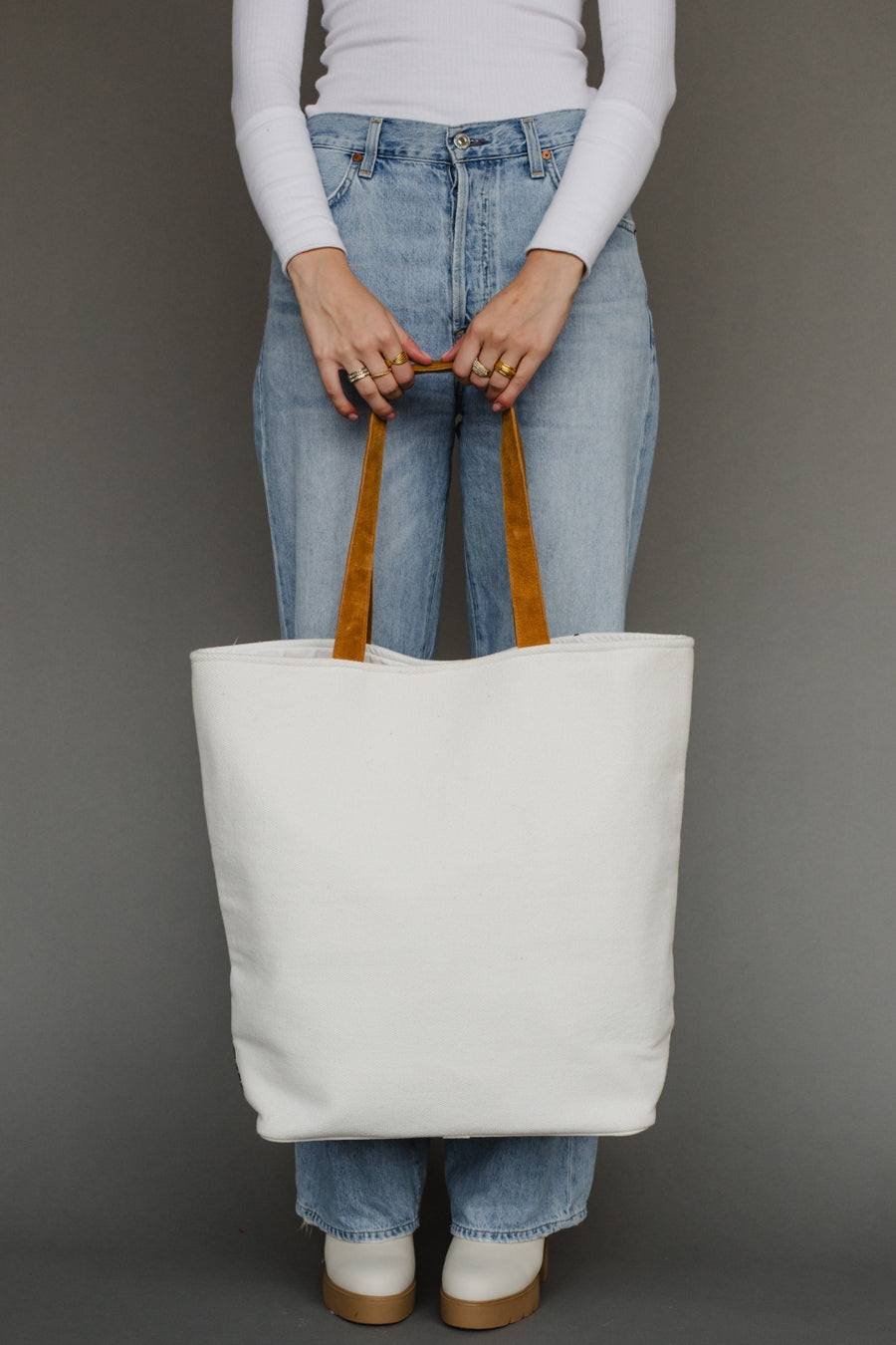 Person holding a white tote bag with brown handles against a gray background