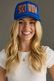 Woman wearing a blue cap with 'SKI BUM' text on a gray background
