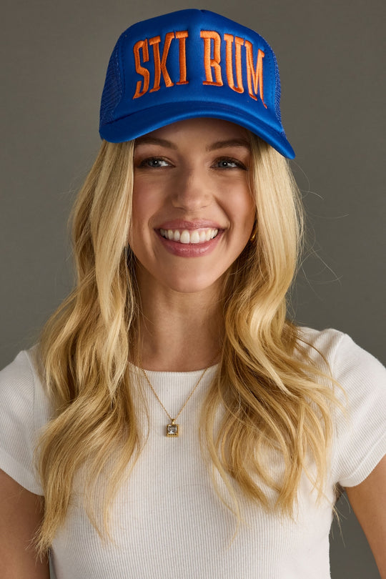 Woman wearing a blue cap with 'SKI BUM' text on a gray background
