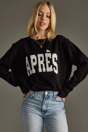 Woman wearing a black sweater with 'APRèS' text and blue jeans against a gray background