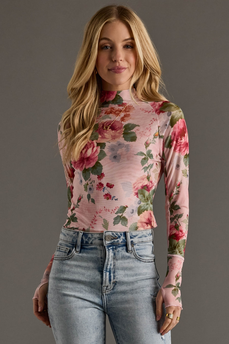 Woman wearing a floral long-sleeve top and jeans against a gray background