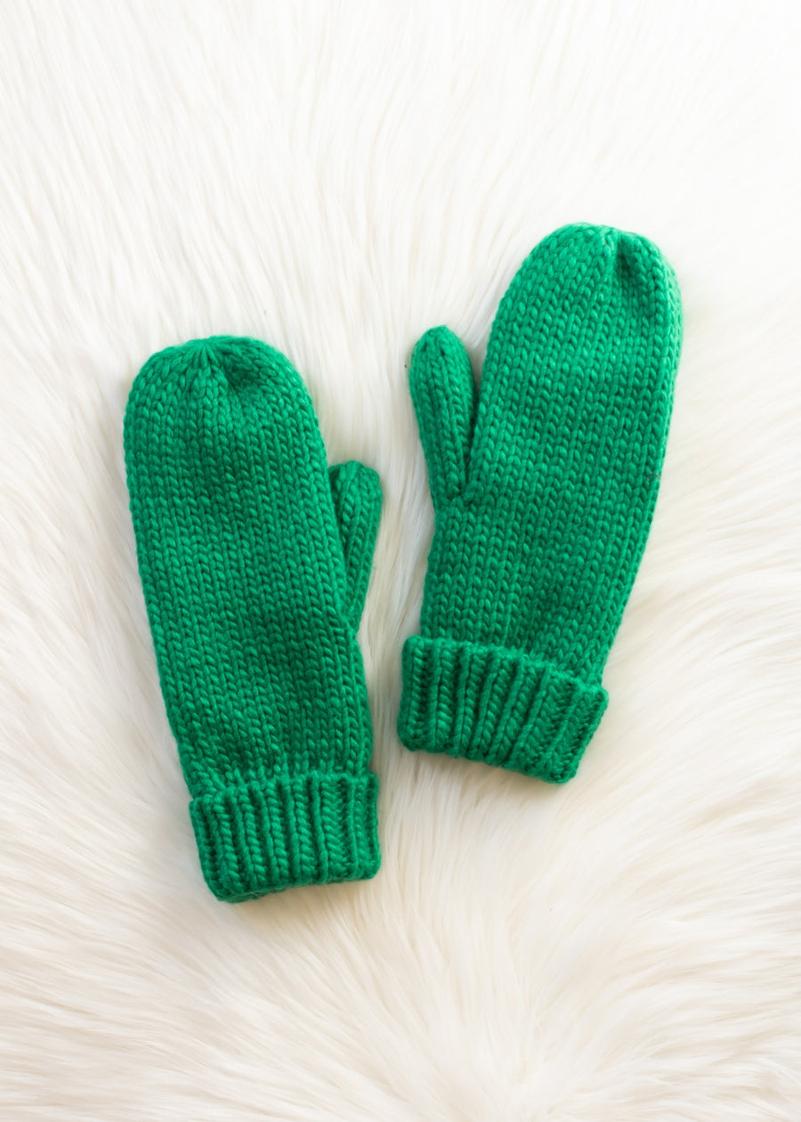Pair of green knitted mittens on a white fur surface