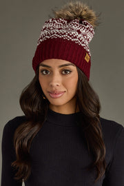 Woman wearing a maroon and white patterned beanie with a pom-pom on a gray background
