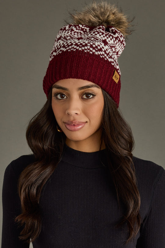 Woman wearing a maroon and white patterned beanie with a pom-pom on a gray background