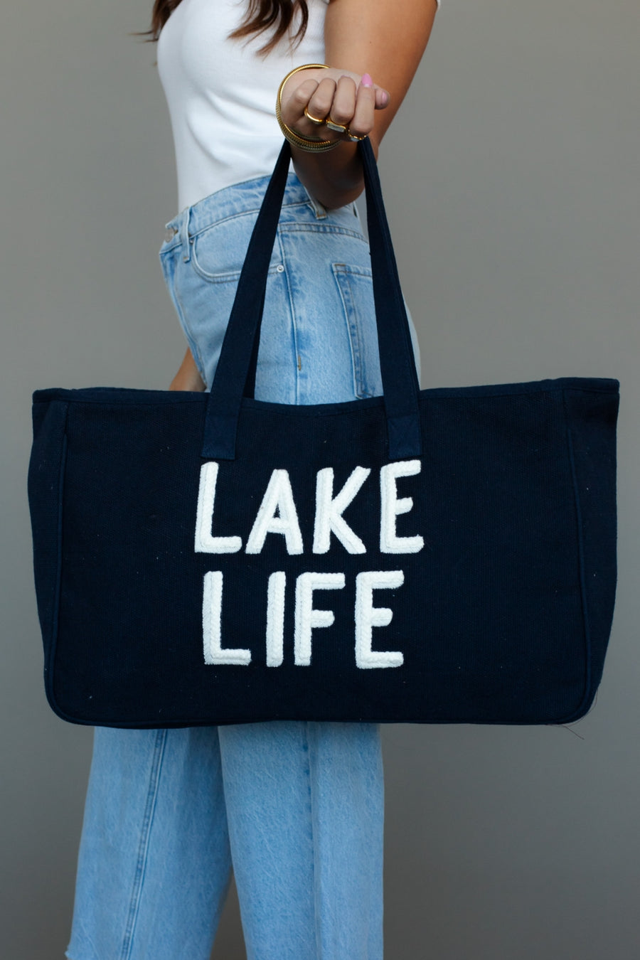 Person holding a black tote bag with 'Lake Life' text against a gray background