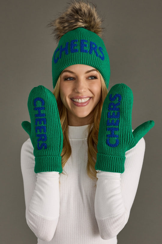 Person wearing green 'CHEERS' beanie and mittens against a gray background