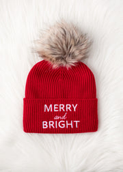 Red beanie with fur pom-pom and 'Merry and Bright' text on a white background