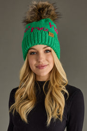 Woman wearing a green knit beanie with a fur pom-pom on a gray background