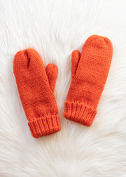 Pair of orange knitted mittens on a white fur surface