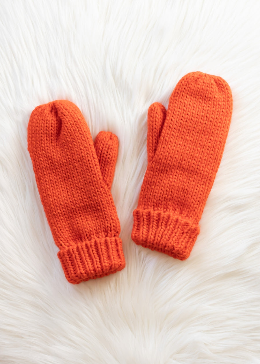 Pair of orange knitted mittens on a white fur surface