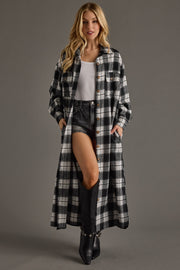 Woman wearing a long plaid coat over a white top and black shorts on a gray background