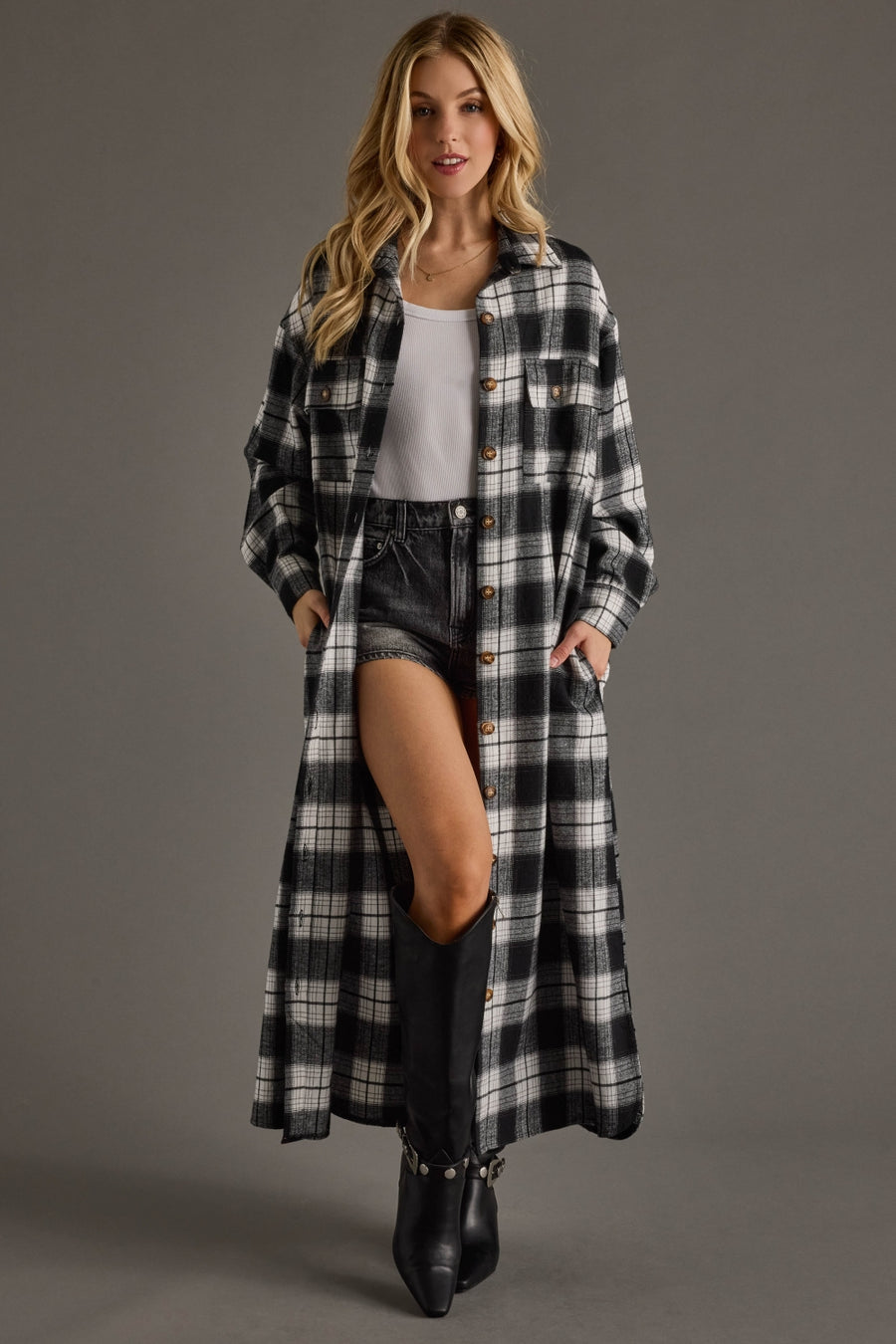 Woman wearing a long plaid coat over a white top and black shorts on a gray background