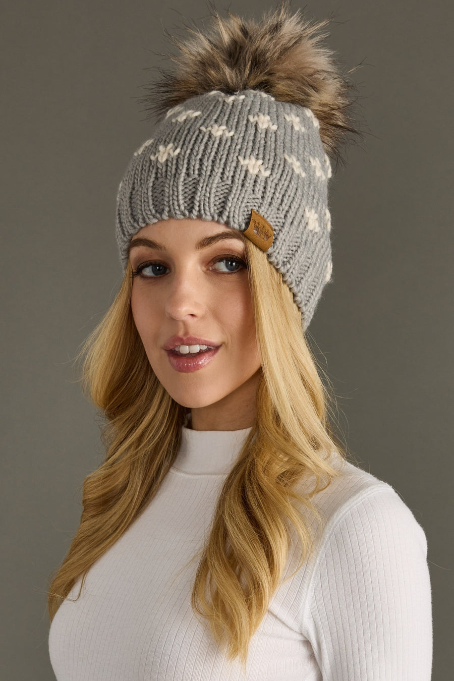 Woman wearing a gray knit beanie with a pom-pom on a gray background