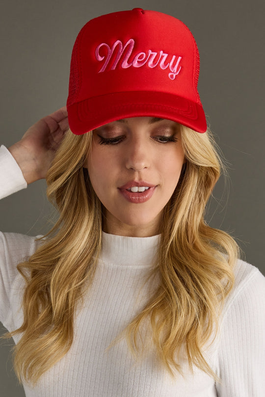 Woman wearing a red trucker hat with 'Merry' text against a gray background