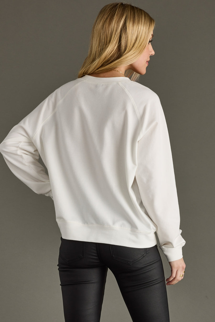 Person wearing a white sweatshirt and black pants against a gray background