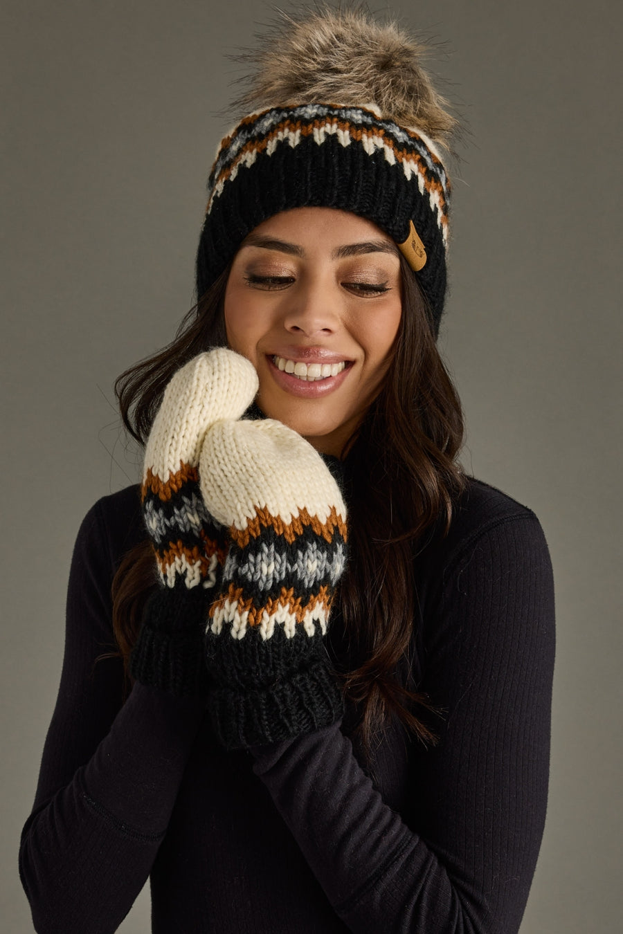 Woman wearing a patterned beanie and mittens against a gray background
