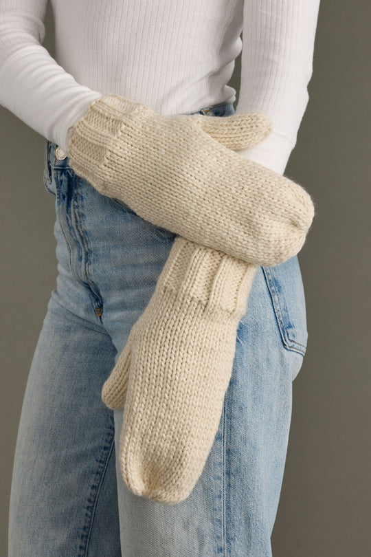 Person wearing beige knitted mittens with a plain background