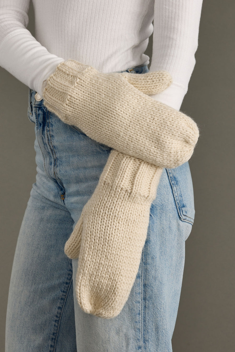 Person wearing beige knitted mittens with a plain background