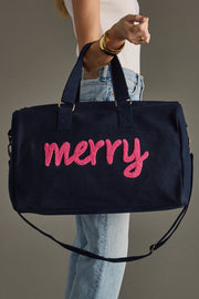 Navy blue bag with pink 'merry' text held by a person wearing jeans and a white top.