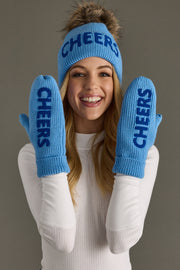 Woman wearing a blue 'CHEERS' beanie and mittens against a gray background