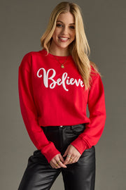 Woman wearing a red sweatshirt with 'Believe' text on a gray background