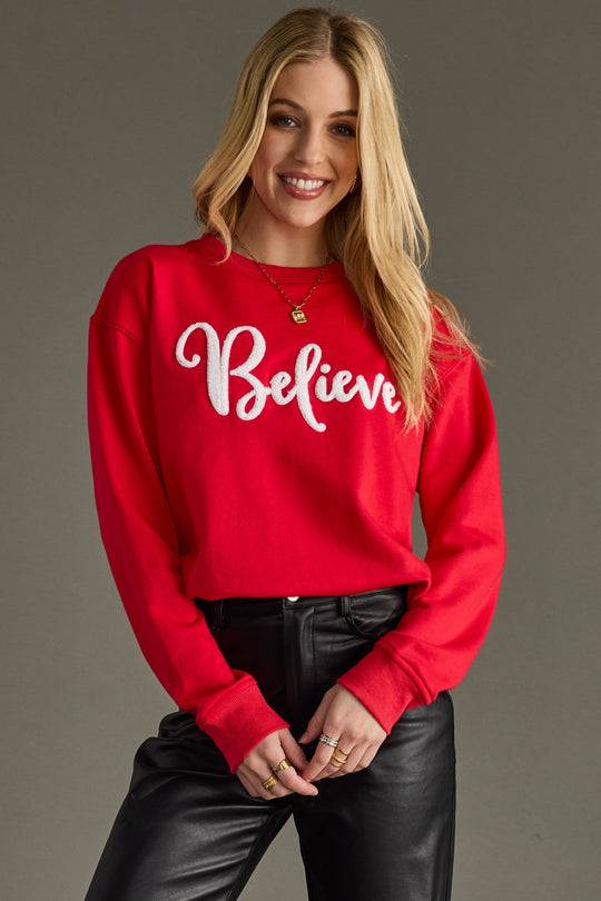 Woman wearing a red sweatshirt with 'Believe' text on a gray background