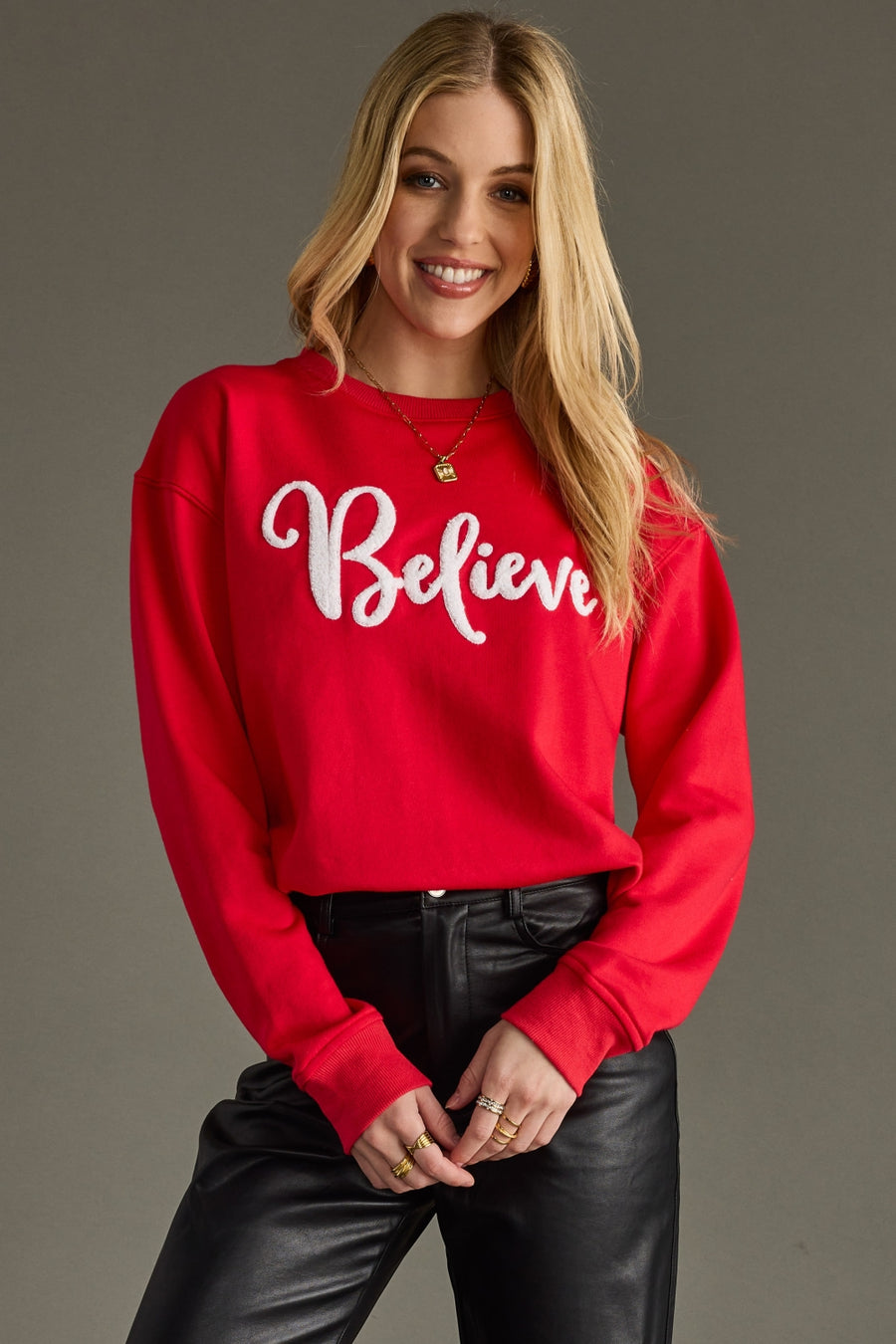 Woman wearing a red sweatshirt with 'Believe' text on a gray background