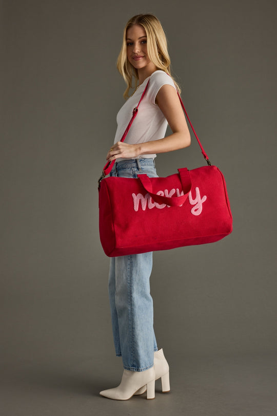Woman holding a red bag with 'merry' written on it against a gray background
