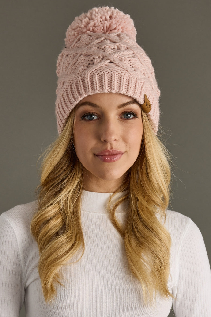 Woman wearing a pink knit beanie with a pom-pom against a gray background