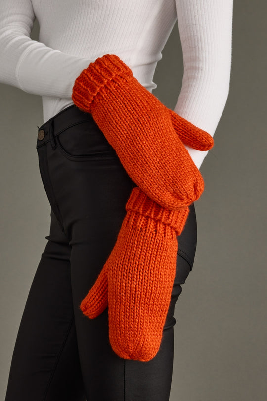 Person wearing orange knitted mittens with a plain background