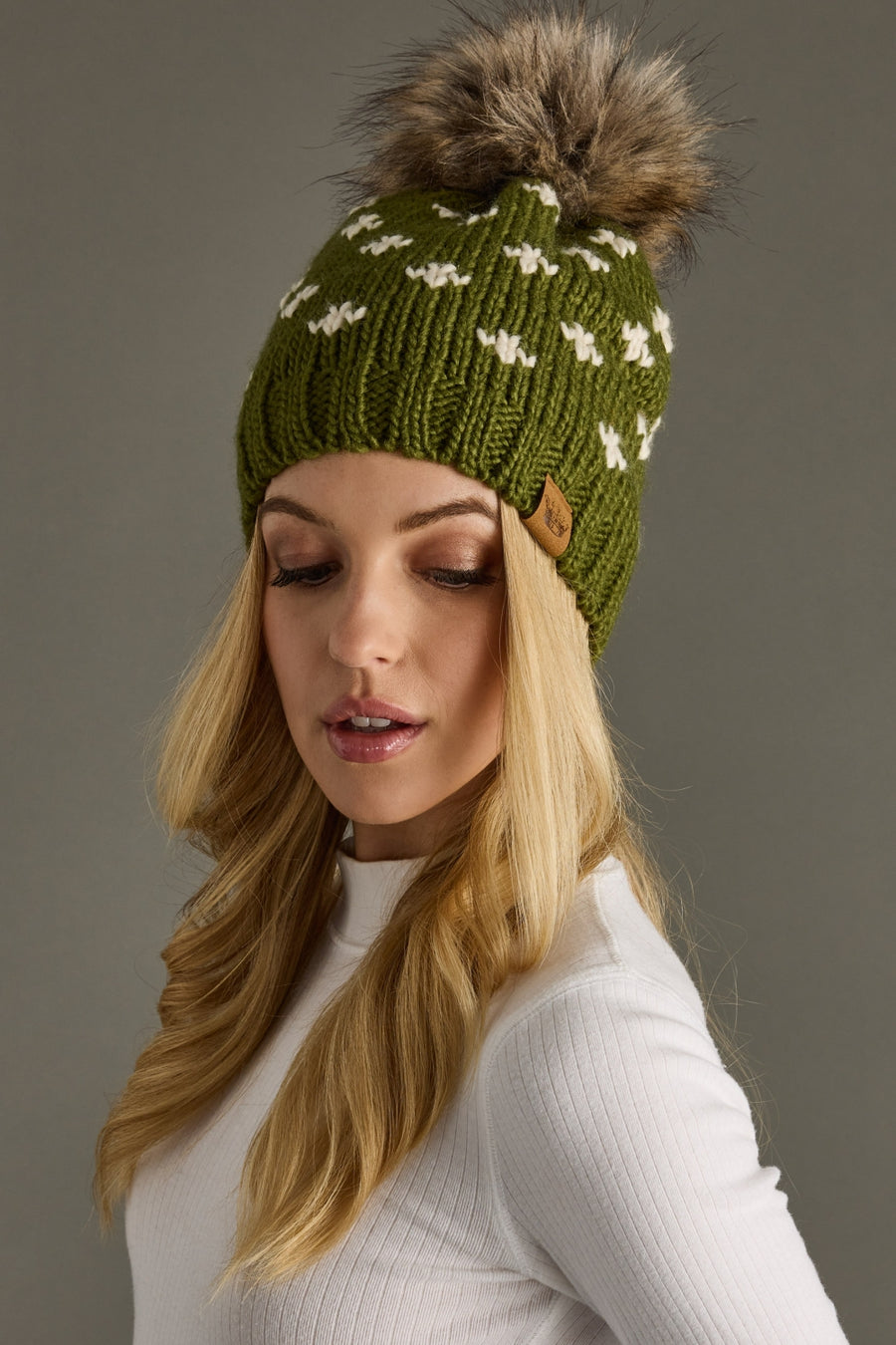 Woman wearing a green knit beanie with a fur pom-pom on a gray background
