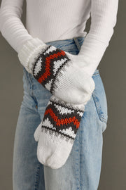 Person wearing white knit mittens with red and black patterns, holding them together.