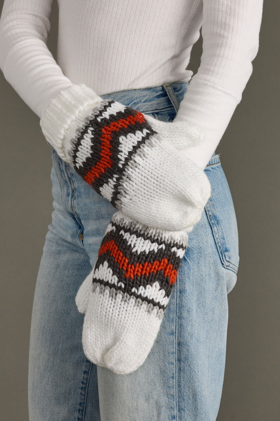Person wearing white knit mittens with red and black patterns, holding them together.