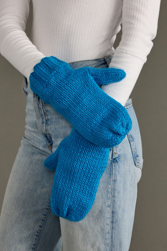Person wearing blue knitted mittens with a plain background
