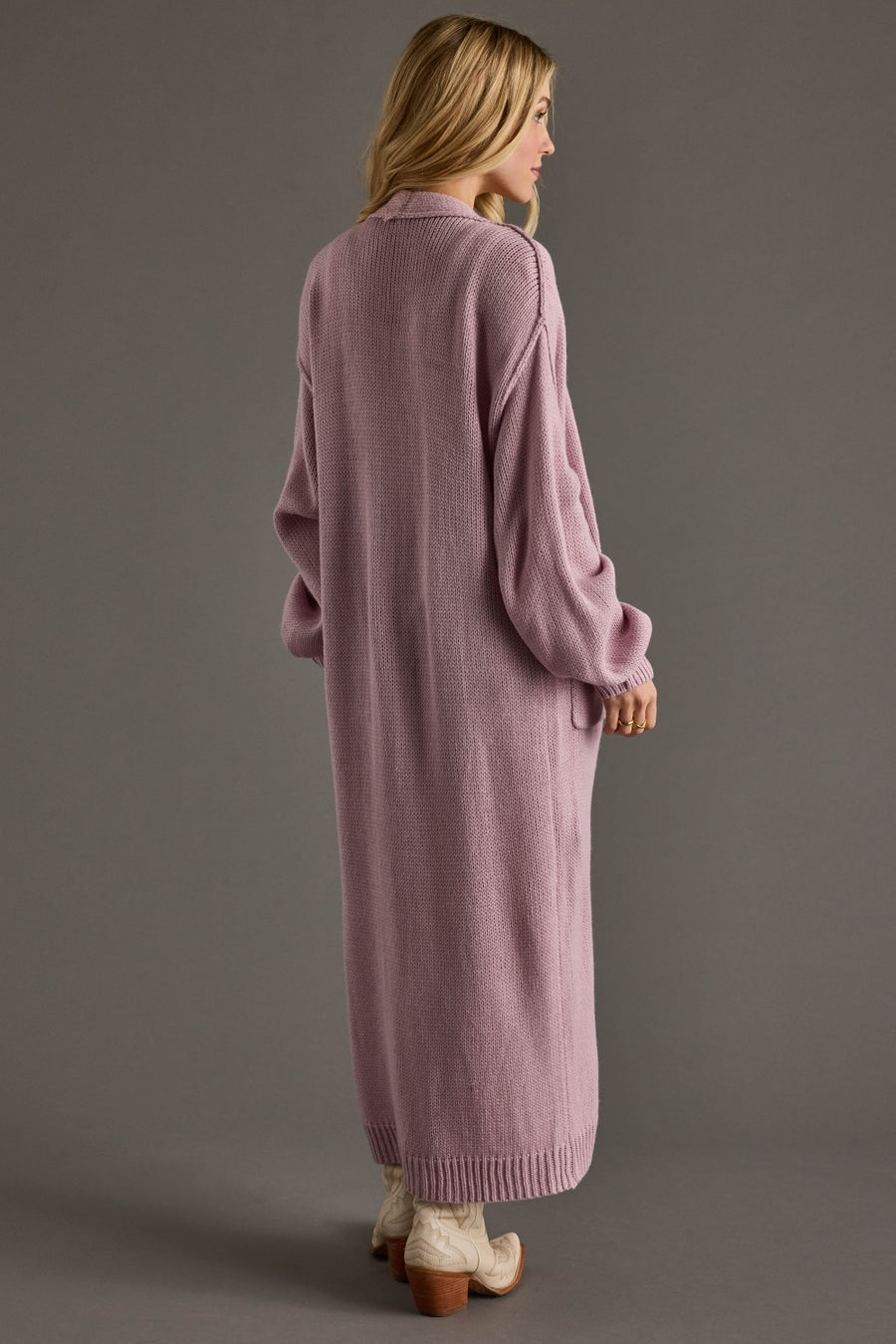 Woman wearing a long pink cardigan against a gray background