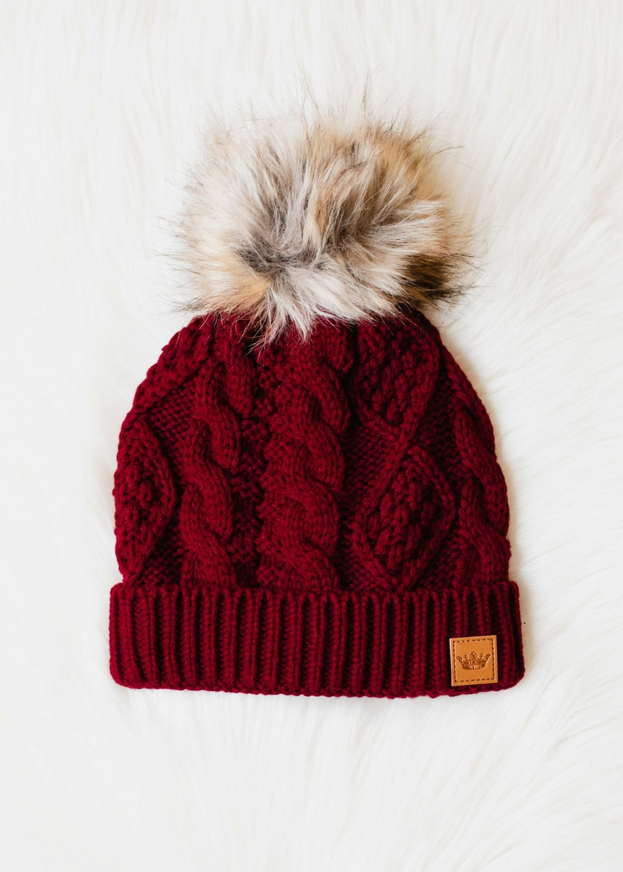 Red knit beanie with fur pom-pom on a white background