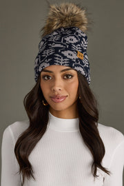 Woman wearing a patterned beanie with a fur pom-pom against a neutral background