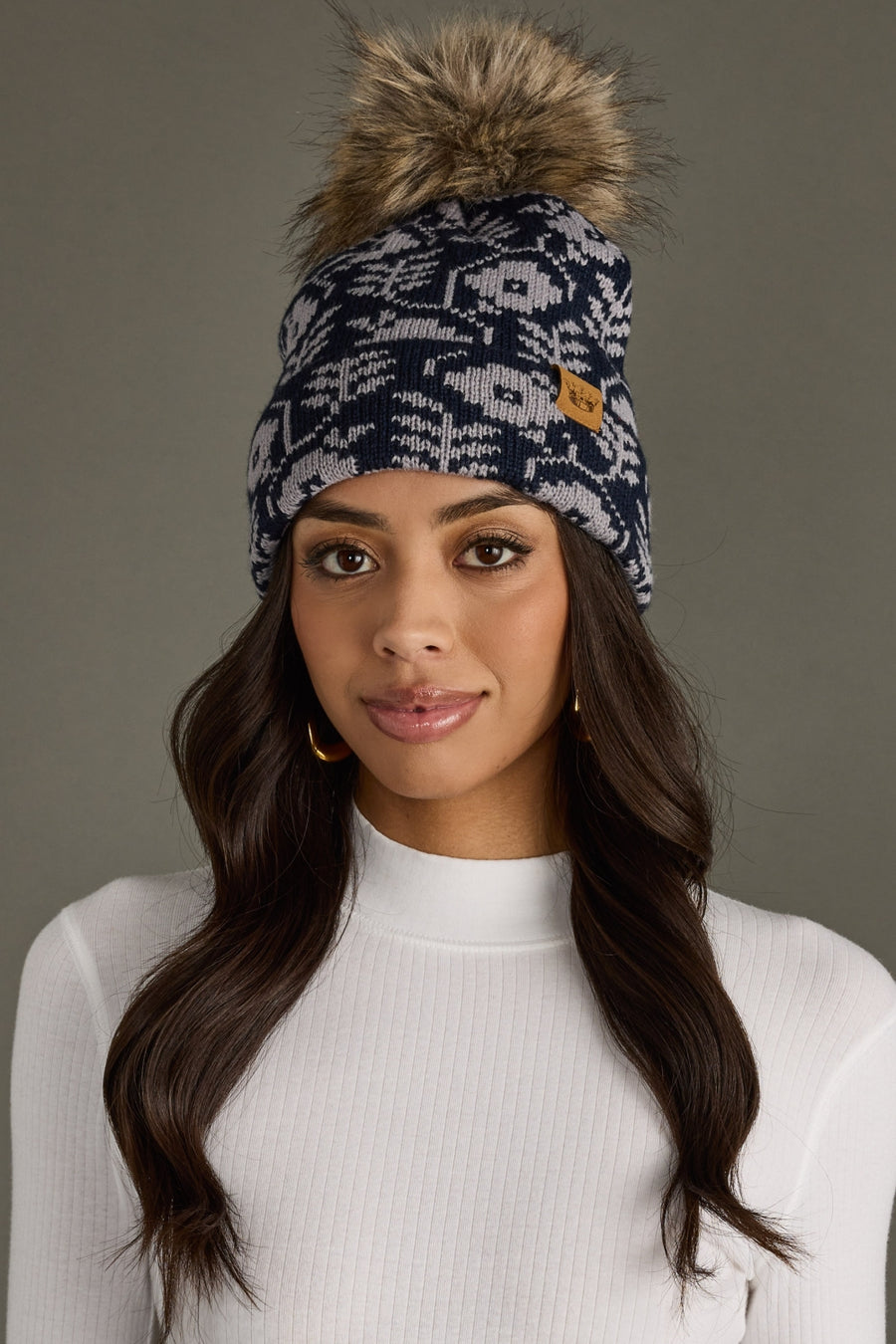 Woman wearing a patterned beanie with a fur pom-pom against a neutral background